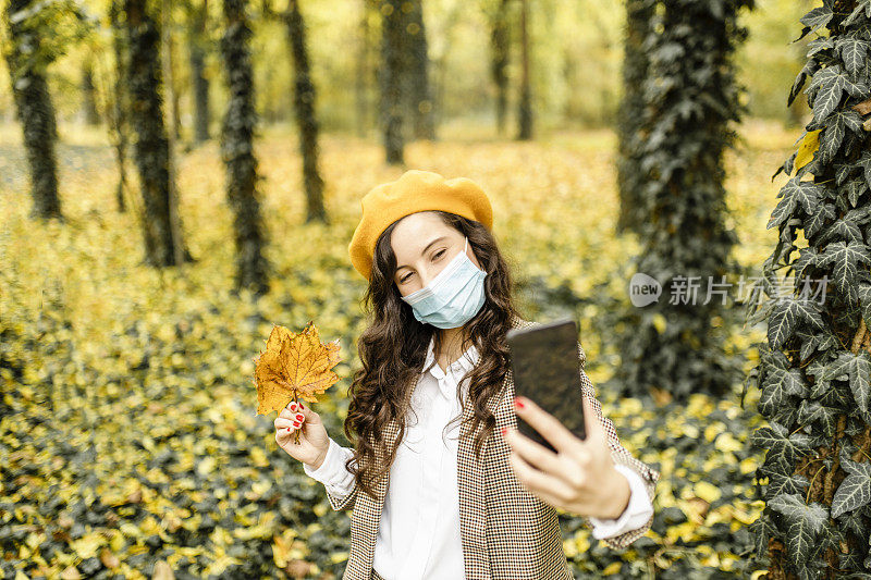 Female fashion blogger using her smart phone and wearing protective face mask during pandemic of coronavirus